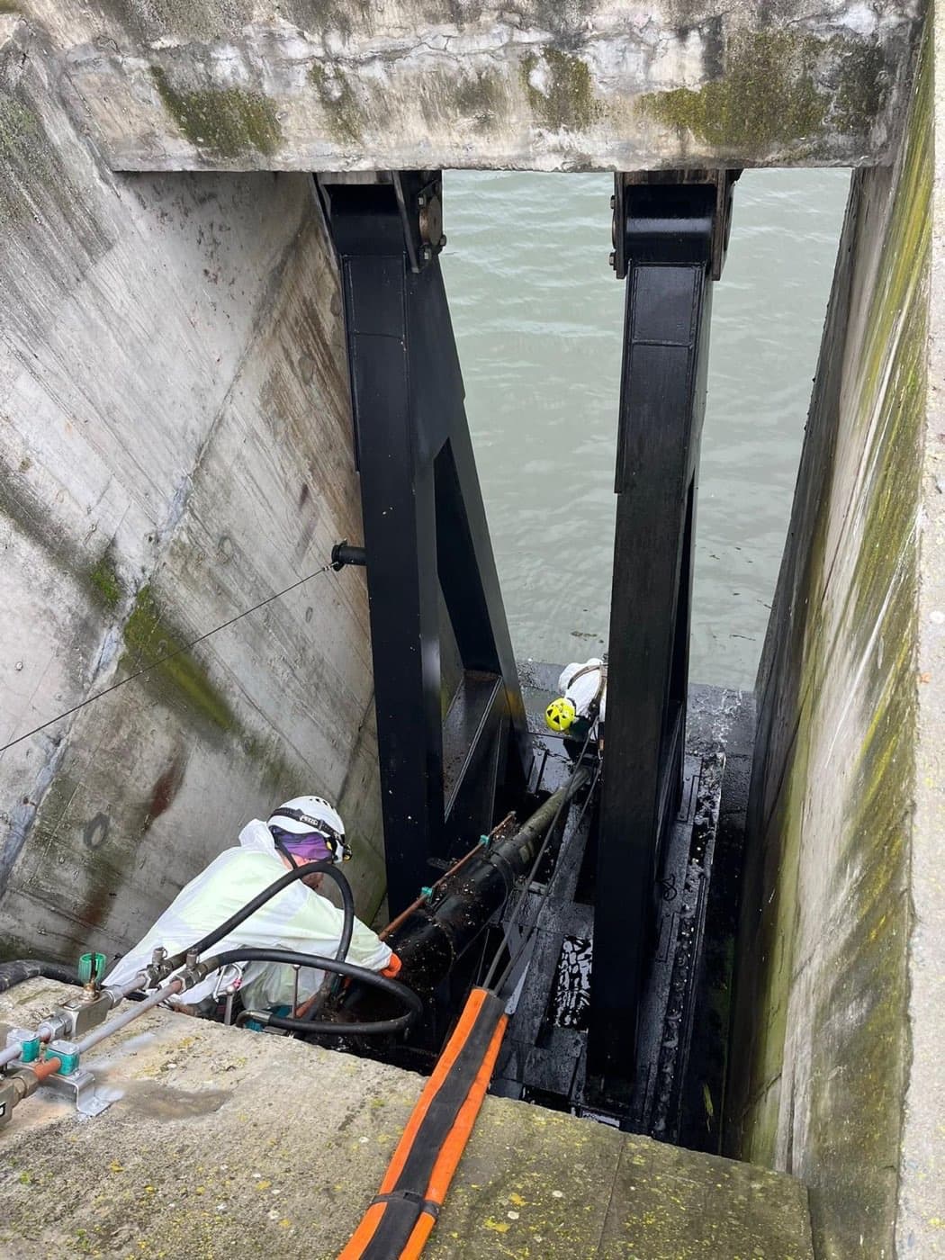 Dois técnicos com equipamento de proteção a intervir na ranhura de uma comporta da barragem.
