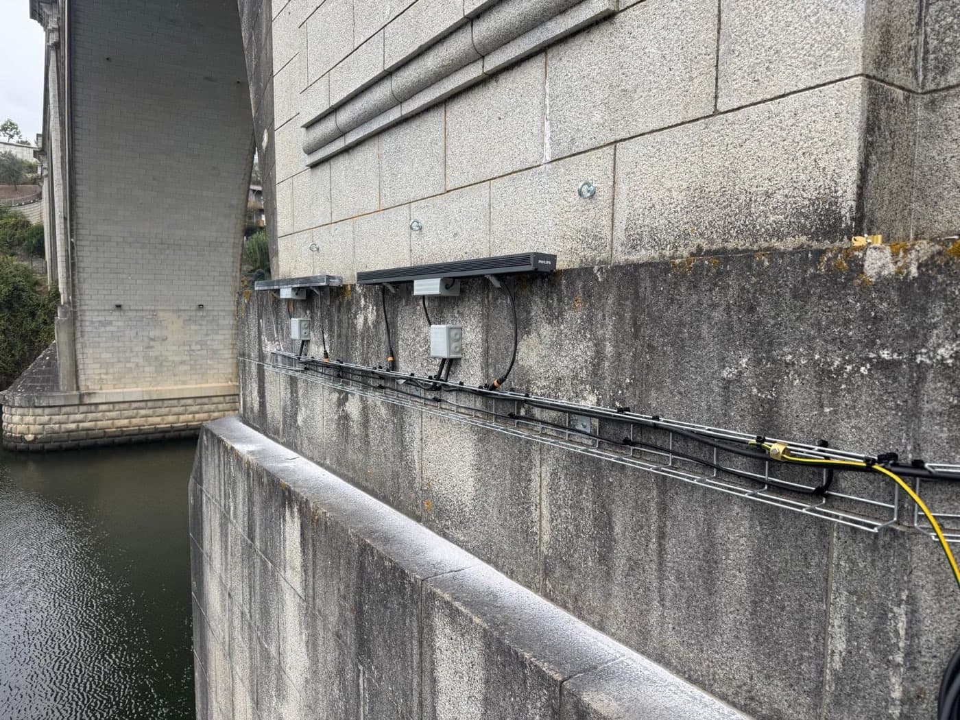 Esteira de cabos e projetores instalados na alvenaria de granito da ponte.