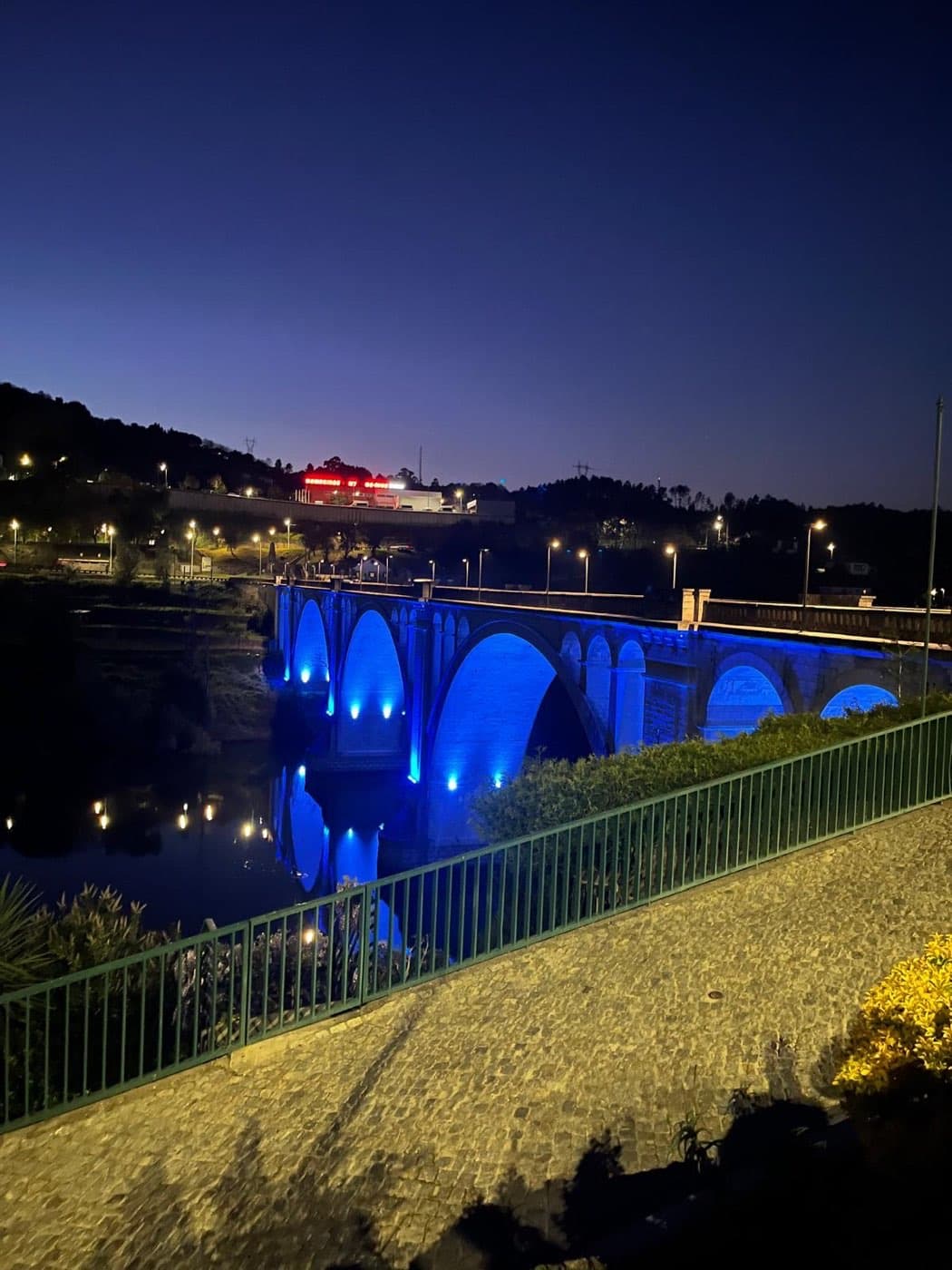 Ponte de granito sobre o rio Douro com a iluminação instalada, ao anoitecer.