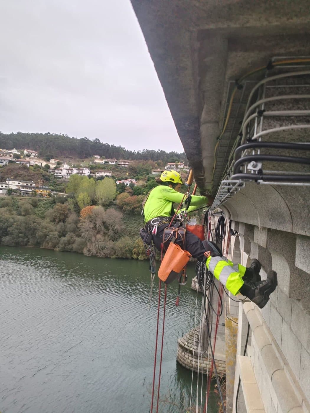 Instalação de equipamento sob o tabuleiro da ponte, em suspensão sobre o rio.