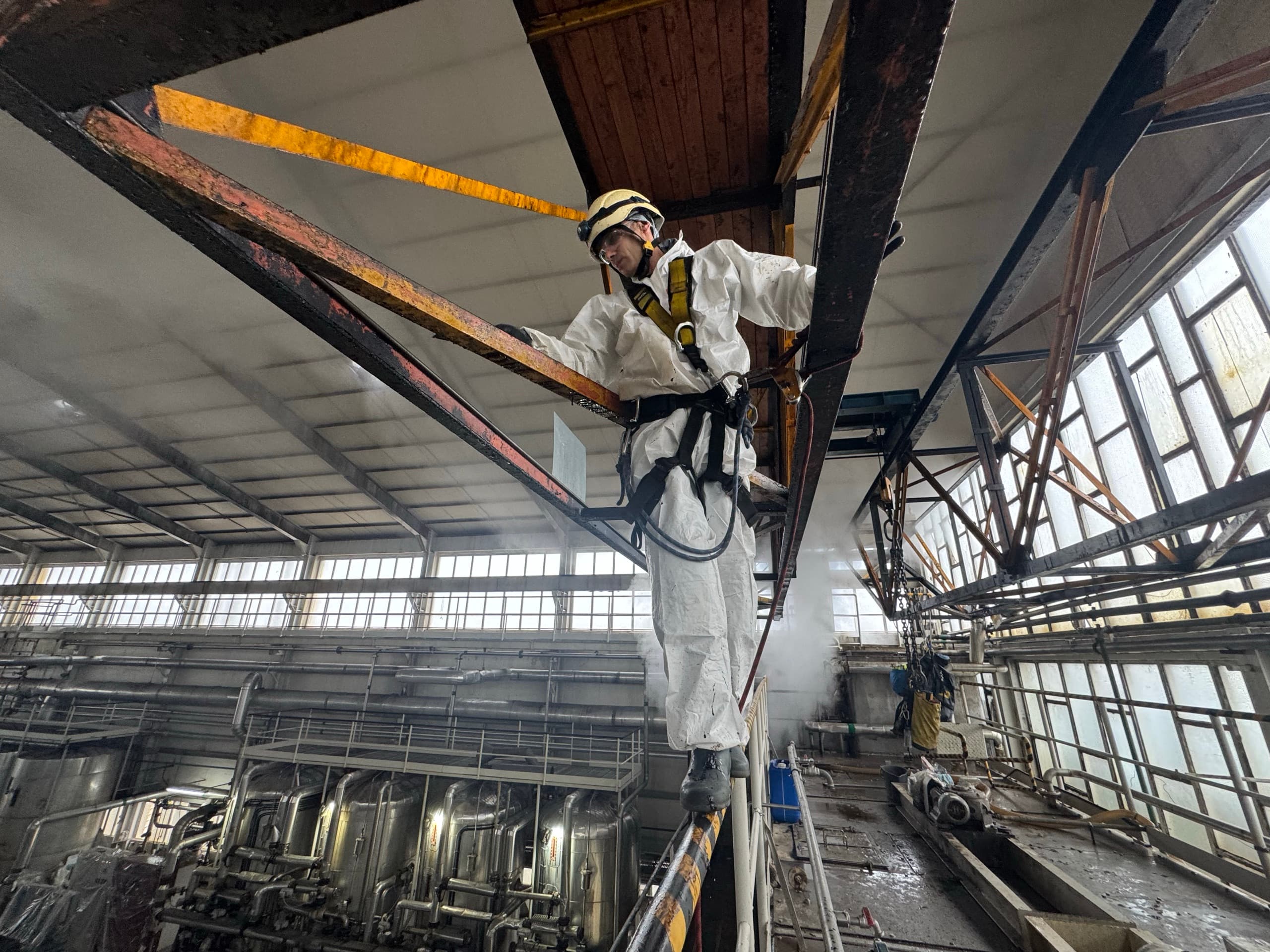 Técnico em suspensão a intervir na estrutura metálica de uma nave industrial no Porto.